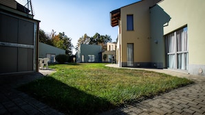 A courtyard with a paved walkway, a grassy area, and buildings with large windows and doors. - Room in Guest Room - Spacious Double Room in Alba (Alba)