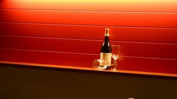 A hotel room with a bed, pillows, a bottle of wine, and a glass on a shelf against a red wall. - Room in Guest Room - Spacious Double Room in Alba (Alba)