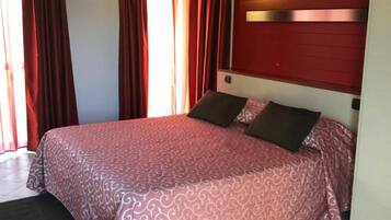 Ein Schlafzimmer mit Bett, Vorhängen, Kopfstütze und Fenster.