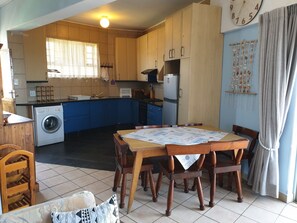 A compact kitchen with a washing machine, a dining table with chairs, and a clock on the wall.