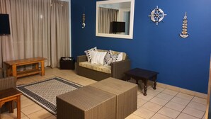 Un salon avec un mur bleu, un canapé, une table basse, un téléviseur et un élément décoratif en forme d’ancre accroché au mur.