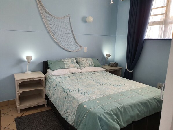 A bedroom with a bed, two bedside tables, a hanging chair, and a window with curtains.
