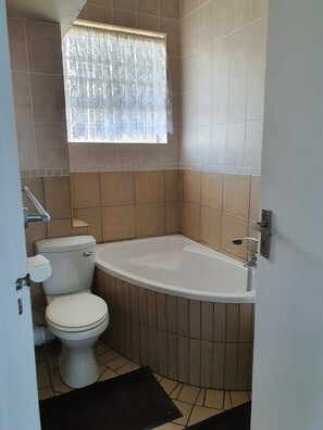 A bathroom with a toilet, a bathtub, and a window with a curtain.