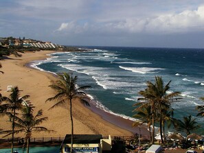 A beach with a resort in the background, a sign for the tourist center, and palm trees along the shoreline.