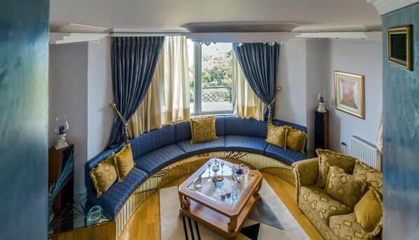 A curved seating area with a glass coffee table, blue and beige sofas, and a view through large windows.