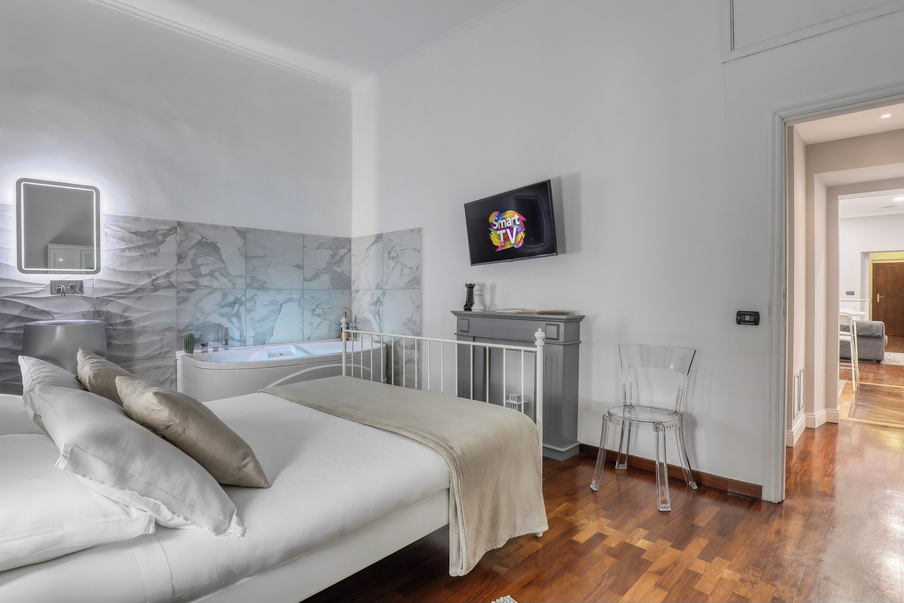 A modern bedroom with a bed, a vanity with a mirror, a TV, and a clear chair.
