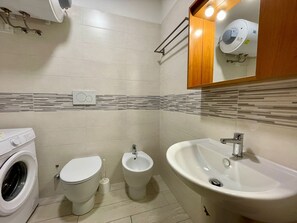 A modern bathroom with a washing machine, toilet, bidet, and sink. - Comfy Flat With Balcony-beahost (Caorle)
