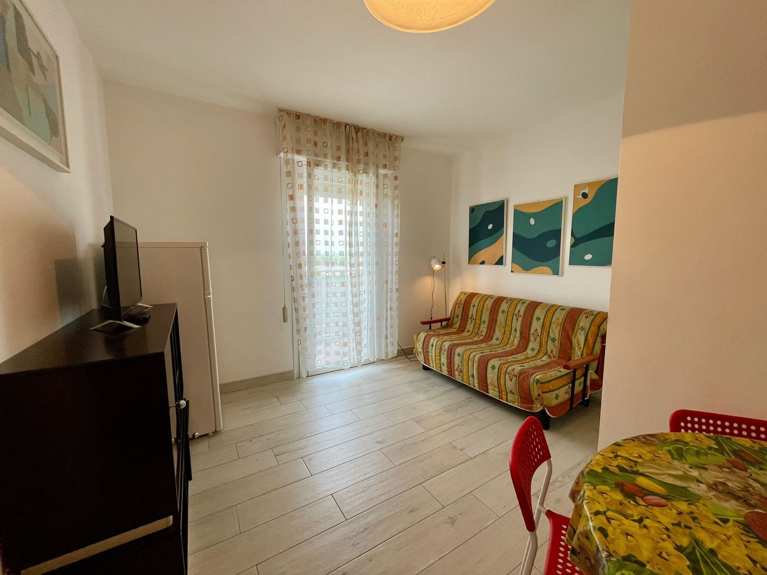 A small, well-lit room with a sofa, a dining table, and a TV on a cabinet.