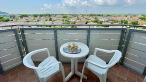 A balcony with two white plastic chairs and a small round table, featuring a tray with bottles and glasses. The balcony overlooks a residential area with houses and greenery. - Comfy Flat With Balcony-beahost (Caorle)
