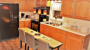 A kitchen with wooden cabinets, a refrigerator, a stove, a sink, and a dining table with chairs. - The Bungalow at Grand Forks (Grand Forks)