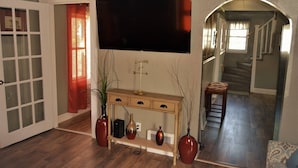 A living room with a flat-screen TV, a console table with vases, a staircase, and a door with frosted glass panels. - The Bungalow at Grand Forks (Grand Forks)