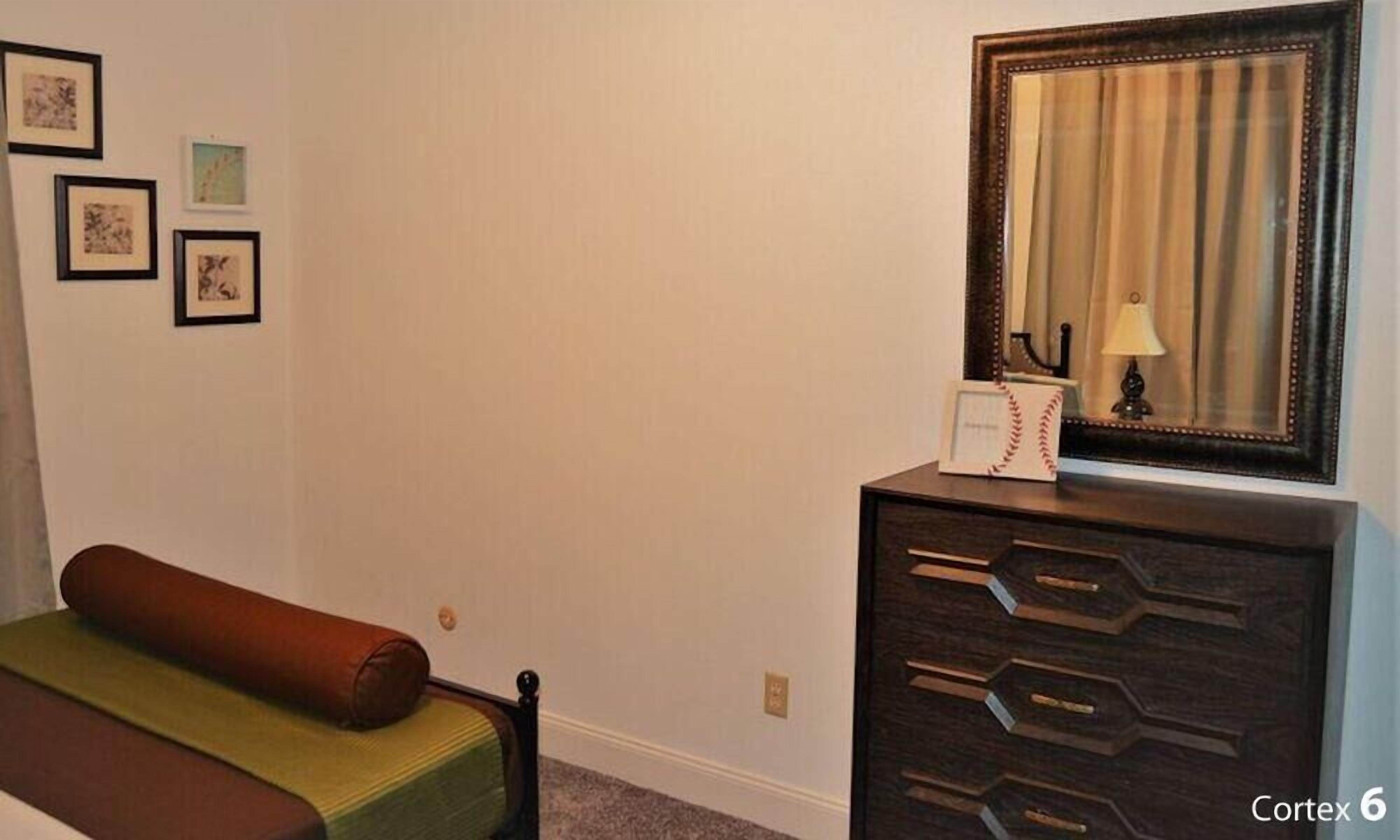 Une chambre à coucher avec un lit, une commode, un miroir et des tableaux encadrés accrochés au mur.