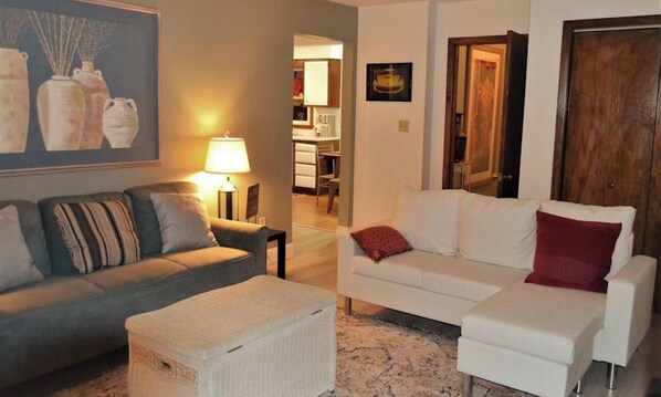A living room with two sofas, a lamp, a painting, and a door. - Arhaus 2 - Riverside Park (Grand Forks)