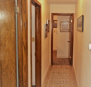 A hallway with wooden doors, a carpeted floor, and framed pictures on the walls. - Arhaus 2 - Riverside Park (Grand Forks)