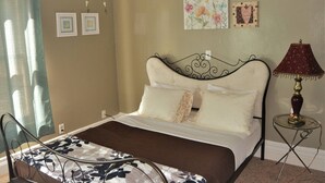 Ein Bett mit Metallgestell, ein Nachttisch mit Lampe sowie eine Wand mit gerahmten Bildern.