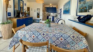A dining area with a patterned tablecloth, wooden chairs, a hanging light fixture, and kitchen cabinets in the background. - Stunning Seafront Apartment (Caorle)