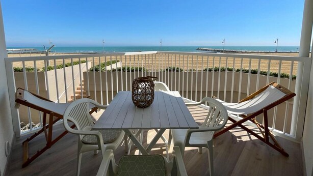 A balcony with a table and chairs, overlooking a beach with a clear sky. - Stunning Seafront Apartment (Caorle)
