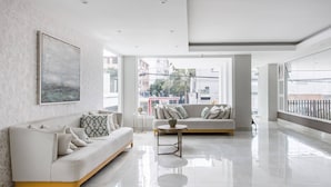 A modern living room with a white sofa, a coffee table, and a large window offering a city view. - Luxurious Apartment In The Heart Of Santo Domingo (Santo Domingo)