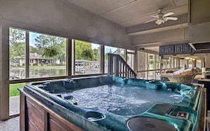 Un jacuzzi en una habitación con ventanas amplias, ventilador de techo y vistas a una casa y árboles.