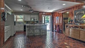 A spacious kitchen with a brick floor, wooden cabinets, a central island with bar stools, and a ceiling fan. - Waterfront Listing - 3 Bedroom 3 Bath on Secluded Private Cove,great Location (Hot Springs)