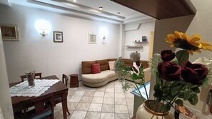 A dining area with a table set for two, a brown sofa with cushions, and a vase with flowers. - Roma Chic House - Luxury Apartment 1 People for Business Studio (Rome)