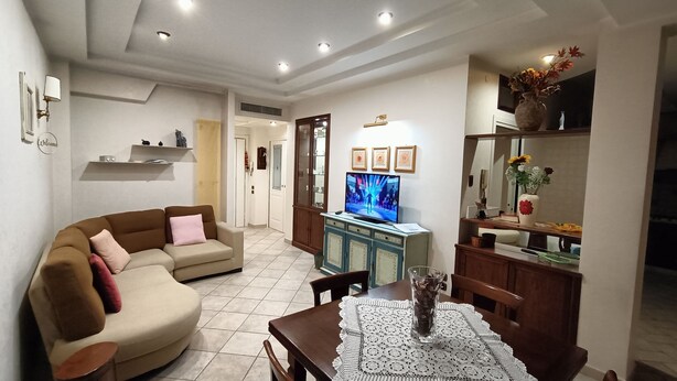 A living room with a sofa, a TV, a dining table with a lace tablecloth, and a vase with flowers. - Roma Chic House - Luxury Apartment 1 People for Business Studio (Rome)