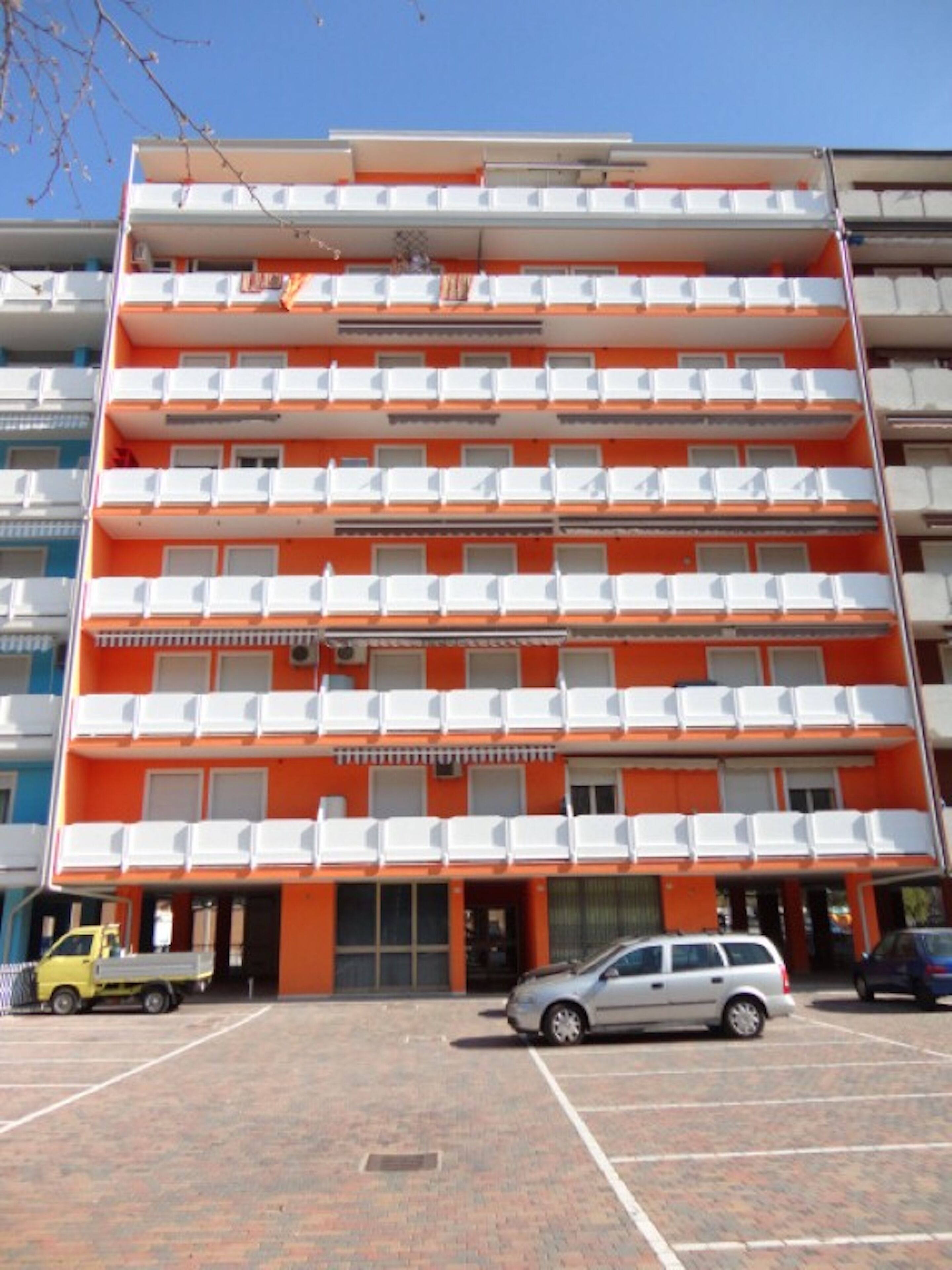 A multi-story building with balconies, a parking lot, and a small entrance area.