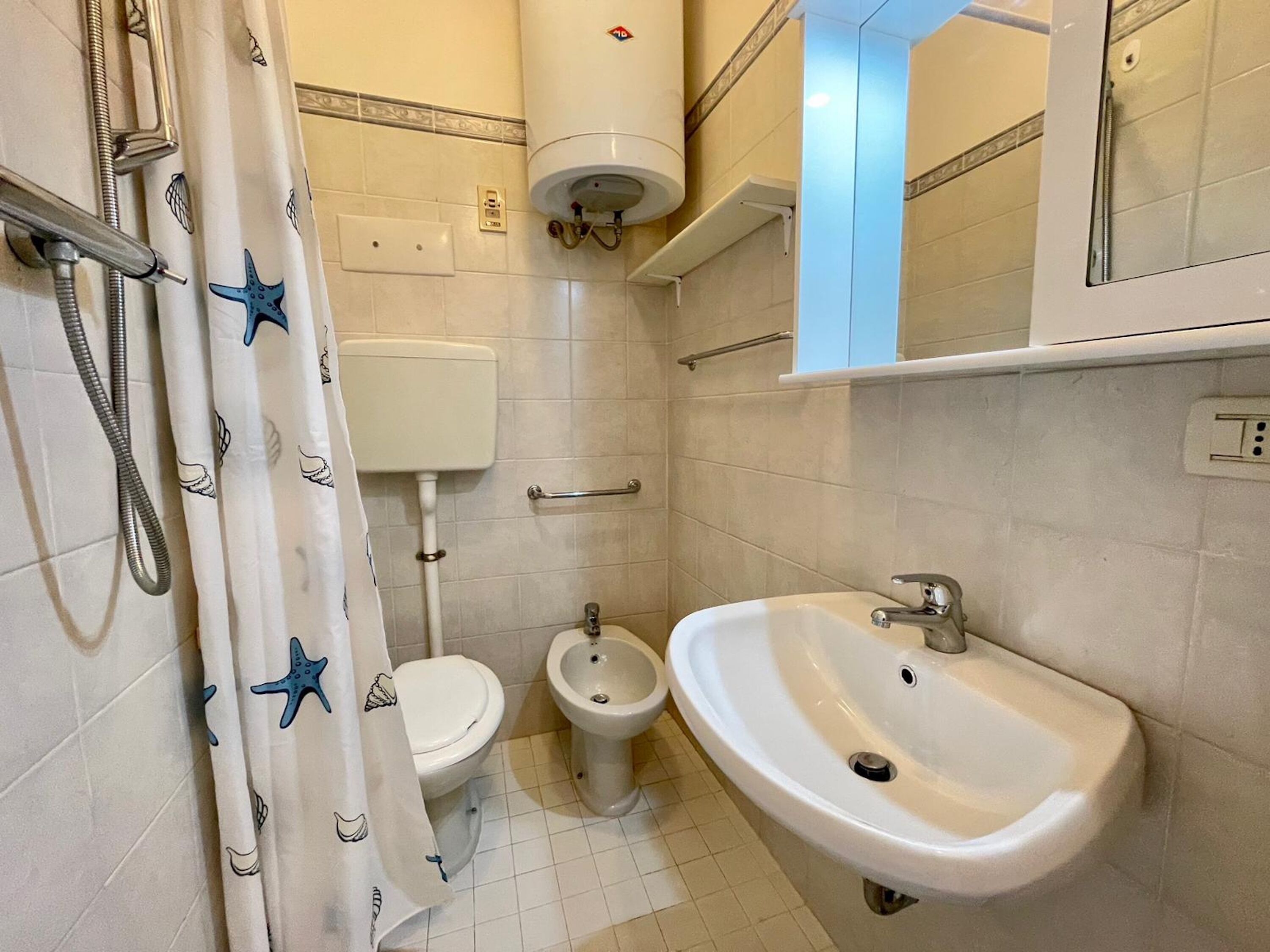 Une salle de bain comprenant des toilettes, un bidet, un lavabo, un rideau de douche orné de motifs d’étoiles de mer et un porte-serviettes.