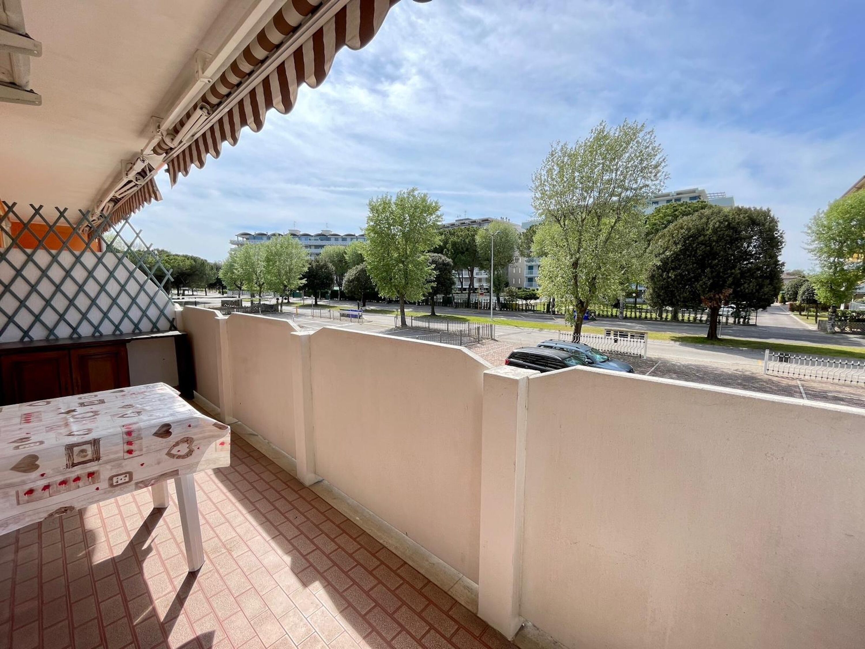 Un balcon avec un sol carrelé, une table avec un journal et une vue sur une rue bordée d’arbres et d’immeubles.