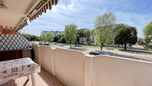 Un balcon avec un sol carrelé, une table avec un journal et une vue sur une rue bordée d’arbres et d’immeubles.