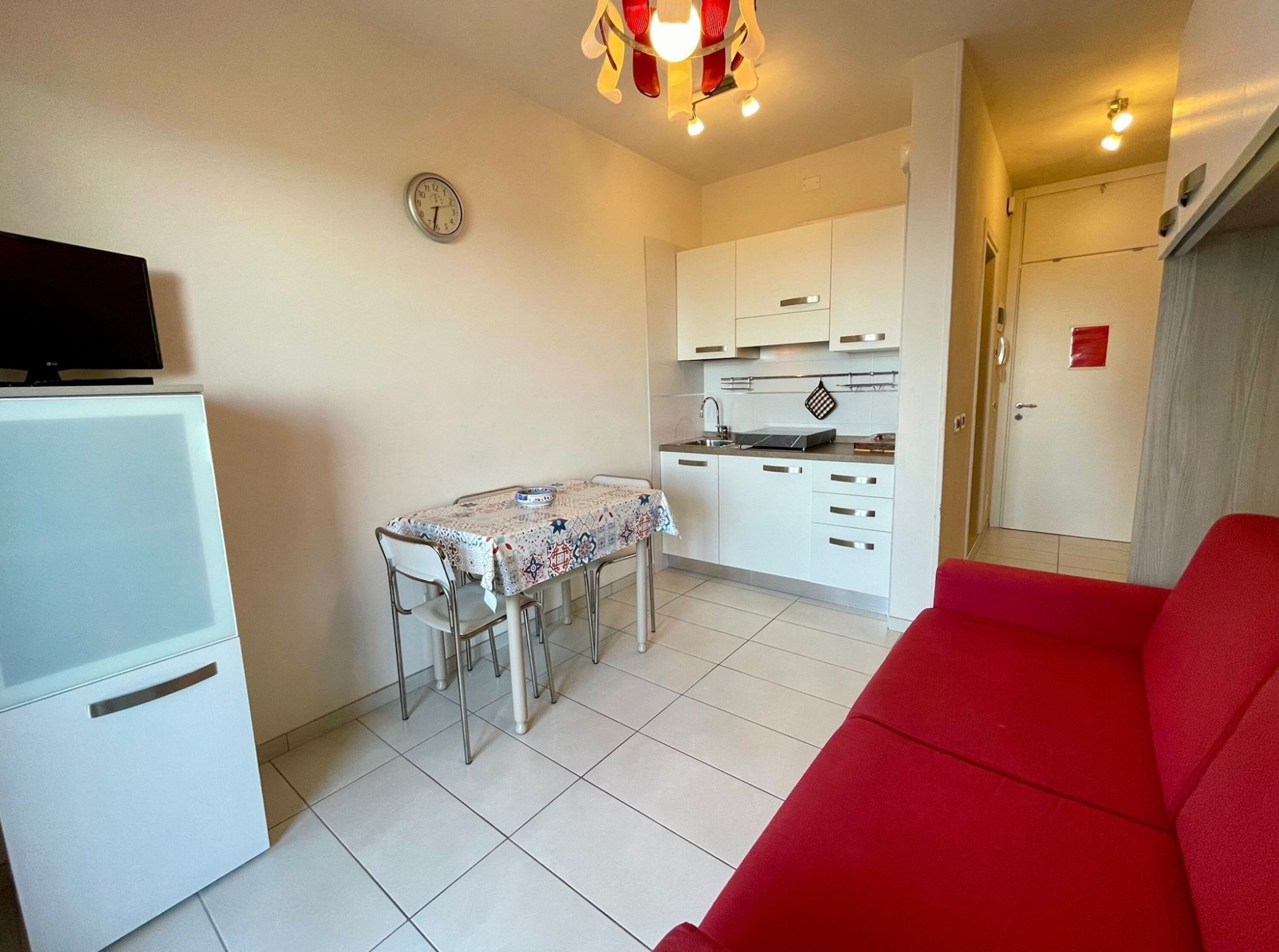 A compact living space with a kitchenette, a dining area, and a red sofa.