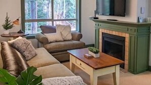 Ein Wohnzimmer mit einer Couch, einem Couchtisch, einem Kamin und einem darüber montierten Fernseher.
