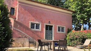 Ein pinkfarbenes Gebäude mit einer Treppe, einem Essbereich mit Stühlen und einem Tisch sowie einem kleinen Garten mit Pflanzen und Blumen.