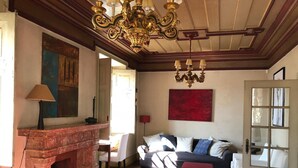 Una habitación con chimenea, un sofá, un reposapiés rojo y una araña.