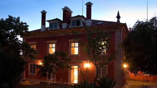 Un edificio de dos pisos con fachada roja, múltiples chimeneas y un jardín bien cuidado.