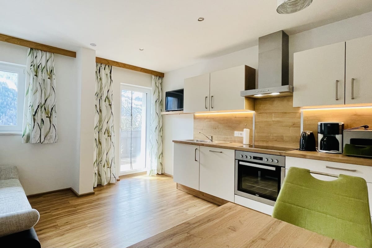 A modern kitchen with wooden cabinetry, a built-in oven, and a dining area with a green chair.