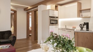 Een moderne keuken met witte kastjes, een ingebouwde oven en een koffiezetapparaat. Er is een zithoek met een rode bank en een tafel met een bloevas.