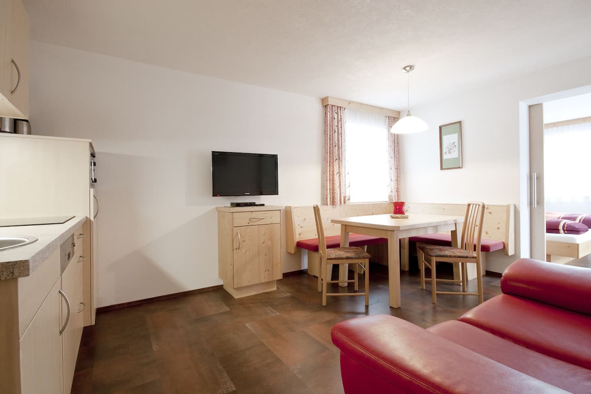 A compact living space with a kitchenette, a dining area with a table and chairs, a red sofa, and a television mounted on the wall.