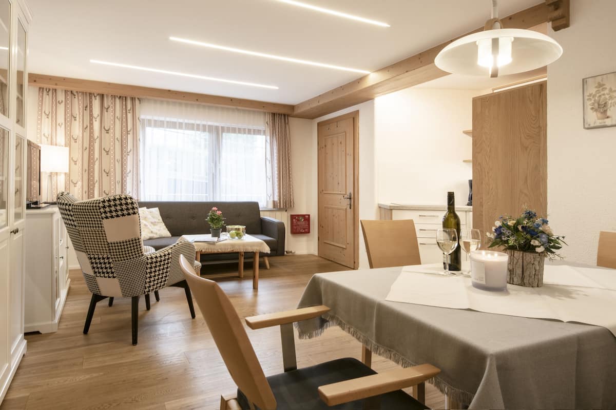 A modern living room with a dining area, wooden flooring, and a large window with curtains.