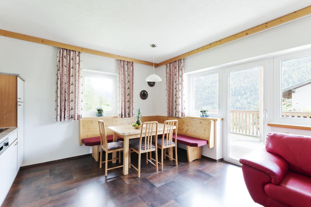 A dining area with a wooden table and chairs, a bench, and a red sofa.