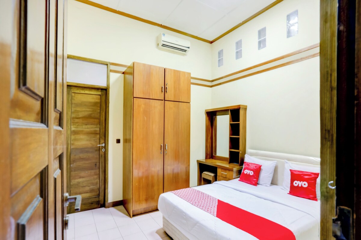 A bedroom with a bed, a wooden wardrobe, a mirror, and a desk.