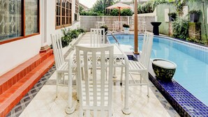 A poolside area with a white table and chairs, a tiled floor, and a pool with blue tiles. - Capital O 90066 Tobana Pejaten House (Jakarta)
