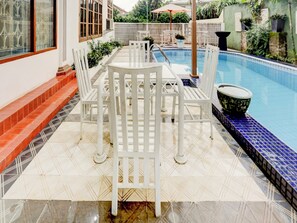 A poolside area with a white table and chairs, a tiled floor, and a pool with blue tiles. - Capital O 90066 Tobana Pejaten House (Jakarta)
