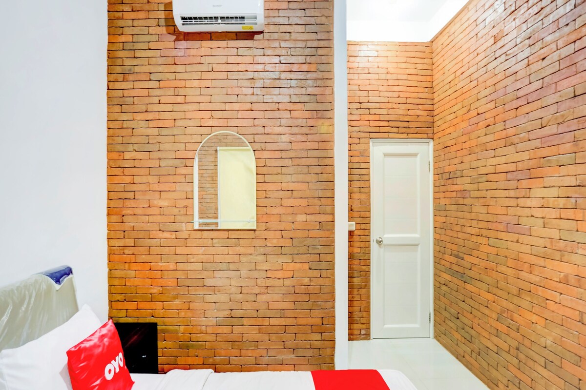 A bedroom with a brick wall, a window, a door, and a bed with a red pillow.