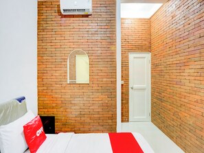 A bedroom with a brick wall, a window, a door, and a bed with a red pillow. - Capital O 90066 Tobana Pejaten House (Jakarta)