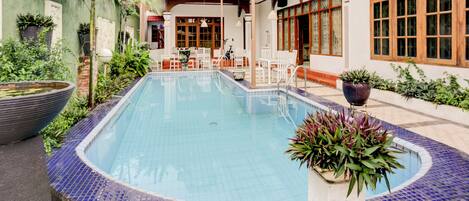A swimming pool with a tiled edge, surrounded by potted plants and a patio area with outdoor furniture.
