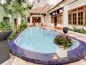 A swimming pool with a tiled edge, surrounded by potted plants and a seating area with white chairs and tables. - Capital O 90066 Tobana Pejaten House (Jakarta)