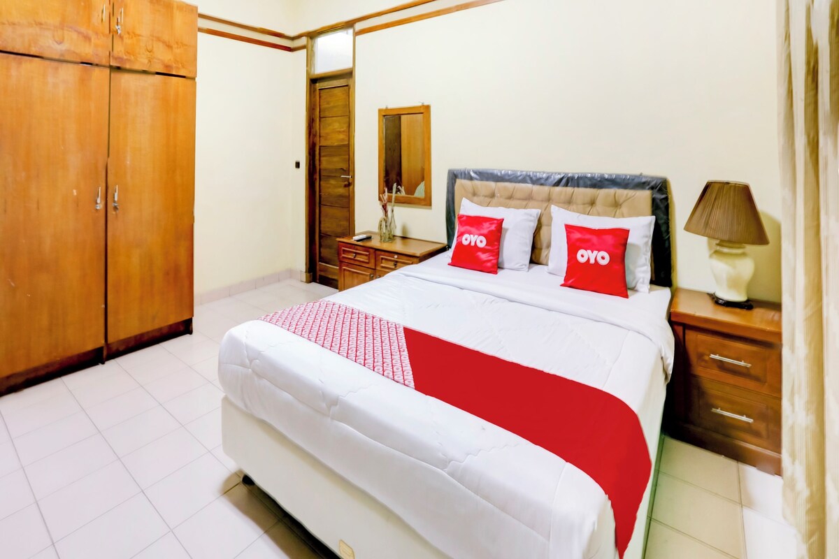 A bedroom with a bed, wooden wardrobe, bedside table, lamp, and a mirror.