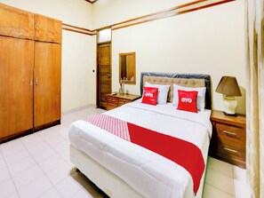 A bedroom with a bed, wooden wardrobe, bedside table, lamp, and a mirror. - Capital O 90066 Tobana Pejaten House (Jakarta)