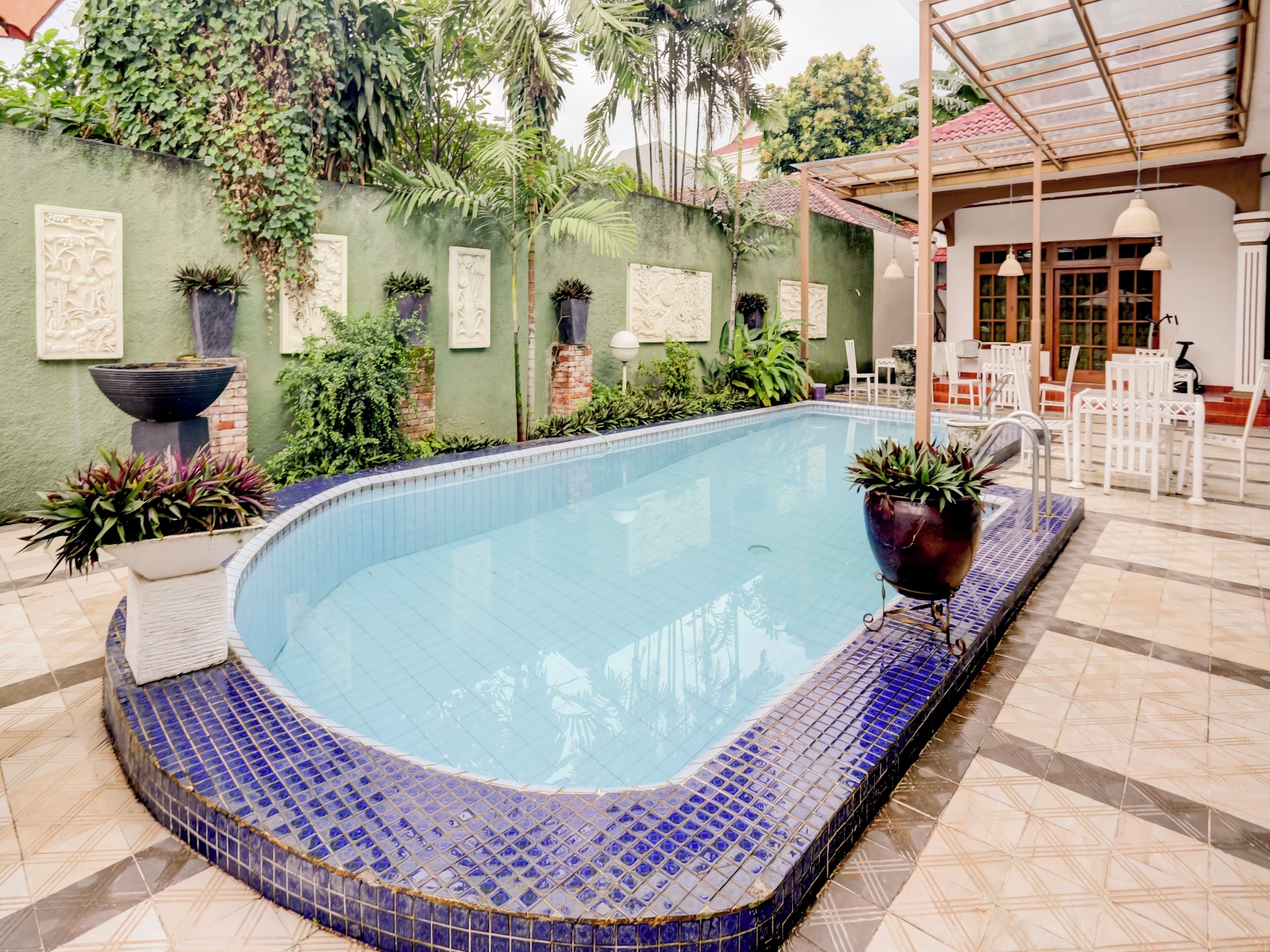 A swimming pool with a tiled edge, surrounded by potted plants and a green wall with decorative panels.